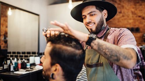 Smiling barber cutting customer's hair in salon.